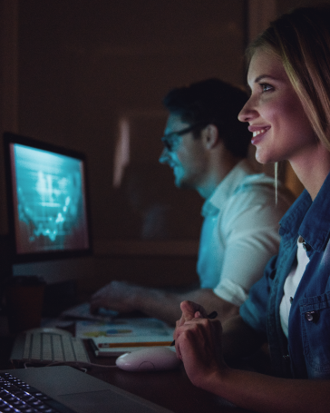 mujer y hombre sentados uno al lado del otro mirando pantallas de computadores